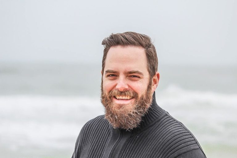 Blog man wearing black zip up jacket near beach smiling at the 736716 768x512