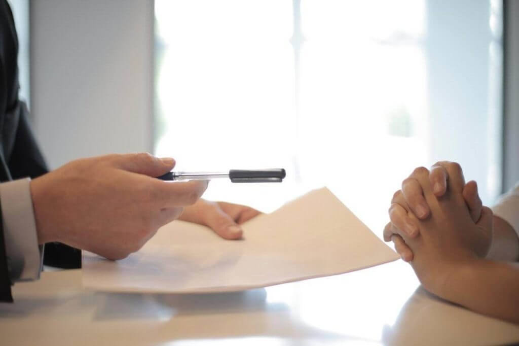 Insurance broker passing contract across desk to physician