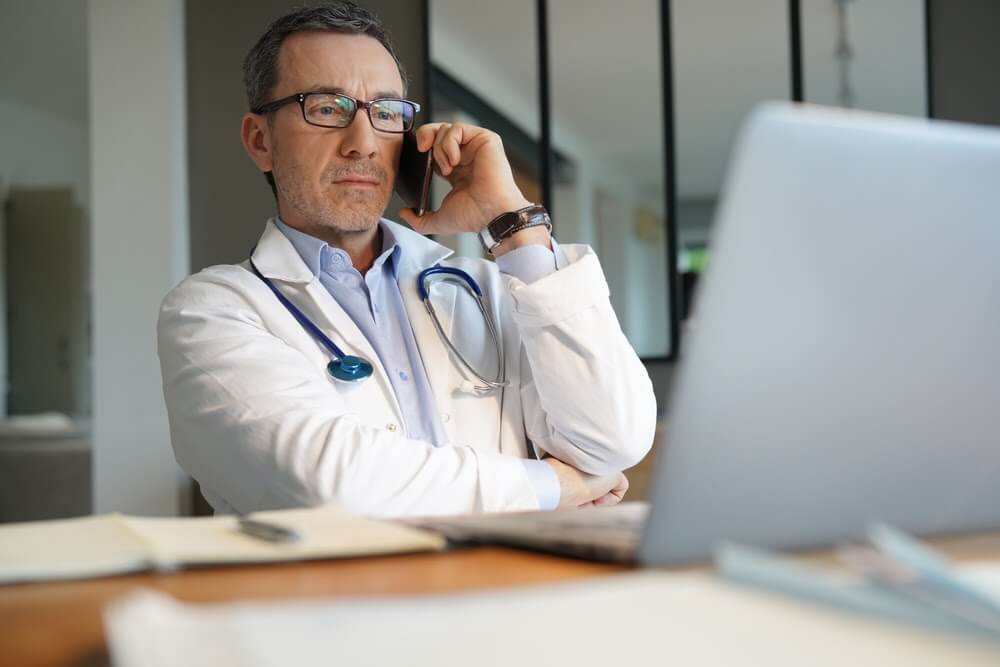 Doctor in office working on laptop talking on phone