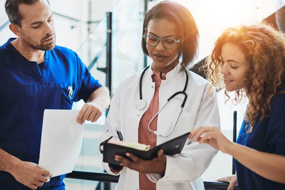 Diverse group of young doctors standing together in a hospital corridor discussing a patient's diagnosis