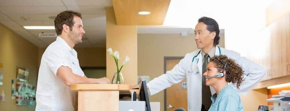 Doctor and nurse talking to man at hospital front desk