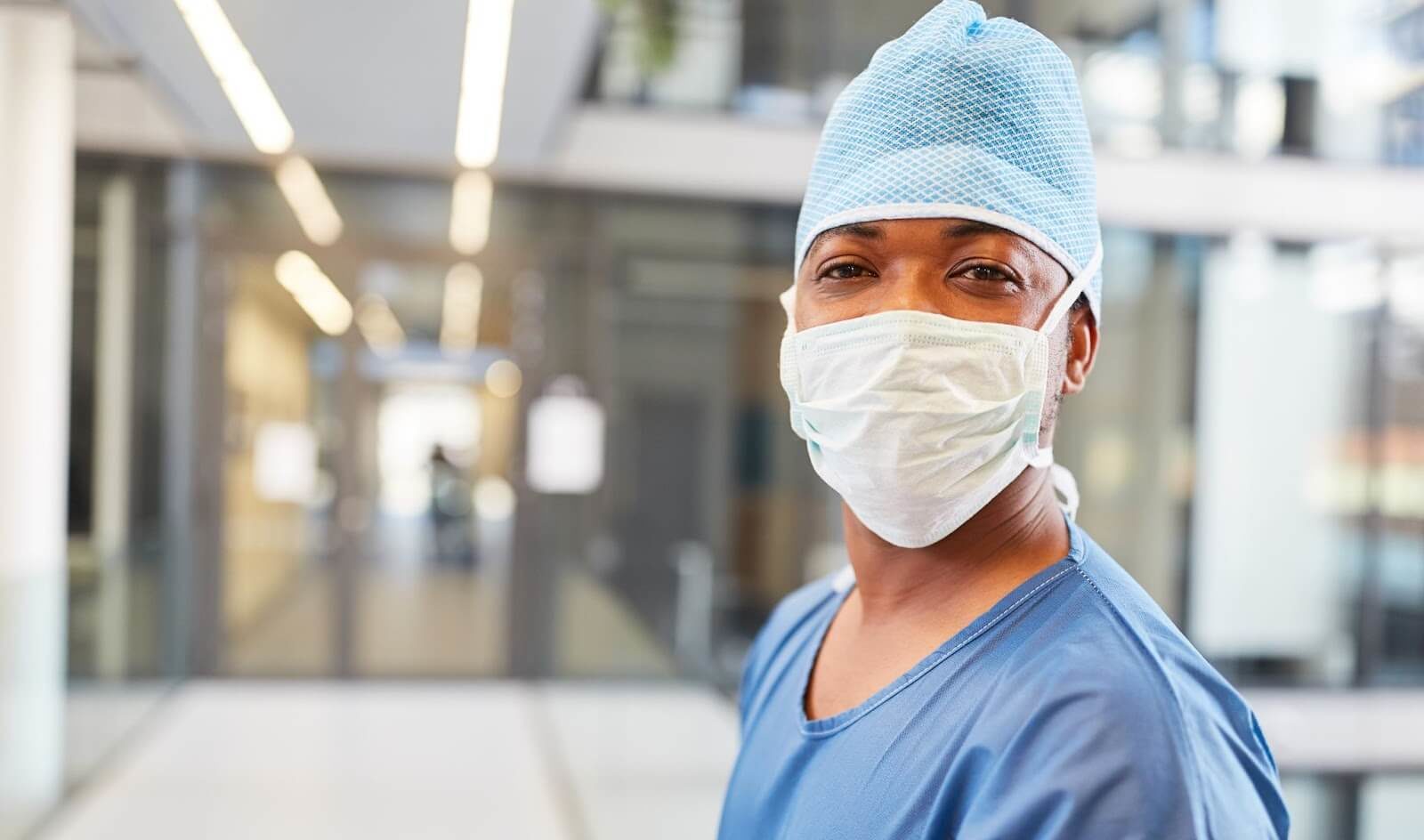 Physician wearing scrubs, hat, and a surgical mask in hospital