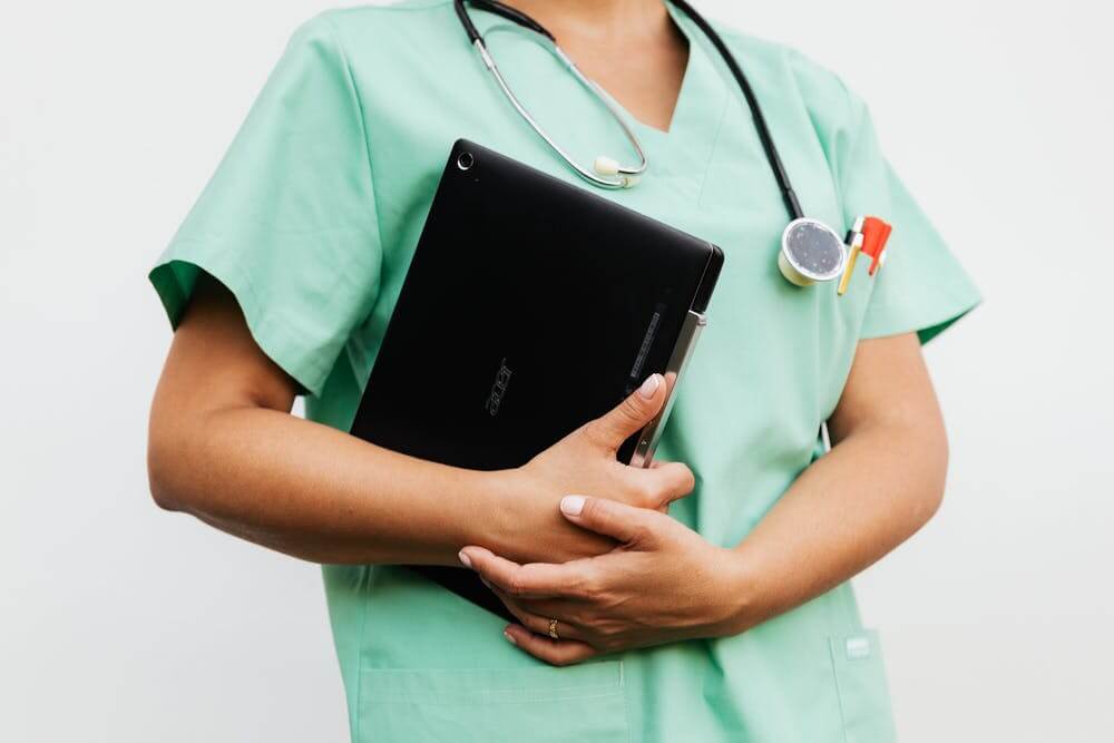 Physician wearing scrubs and stethoscope holding a laptop