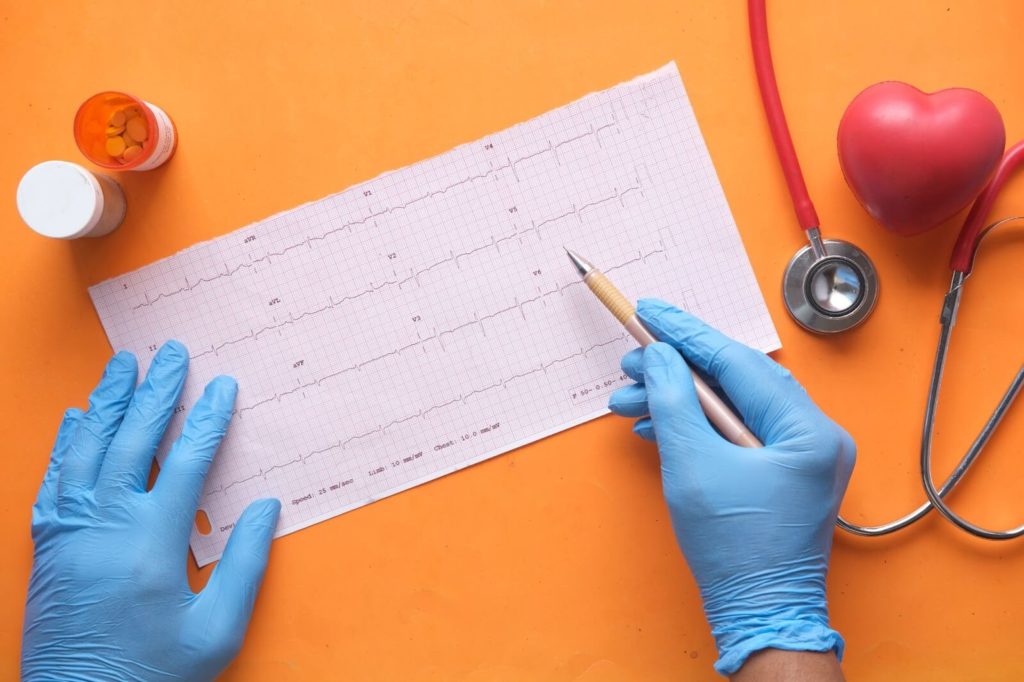 Physician's hands wearing blue rubber gloves and handling heart rate reading paper against an orange background