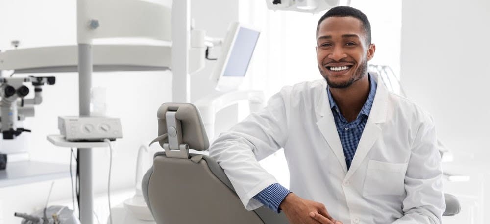 Young black dentist posing at clinic over modern cabinet, empty space